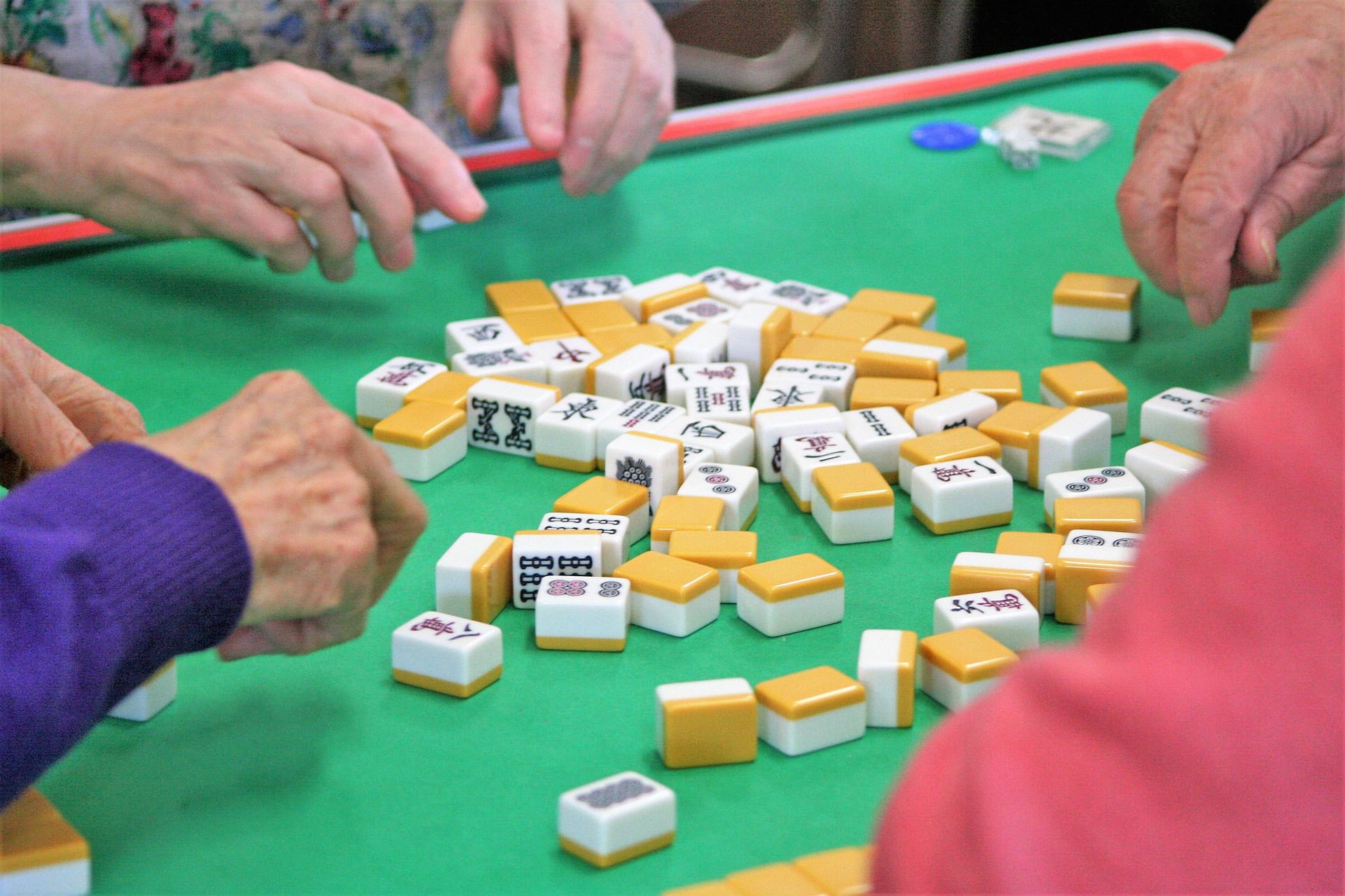 Mahjong tiles in the center of the table with players' hands reaching in